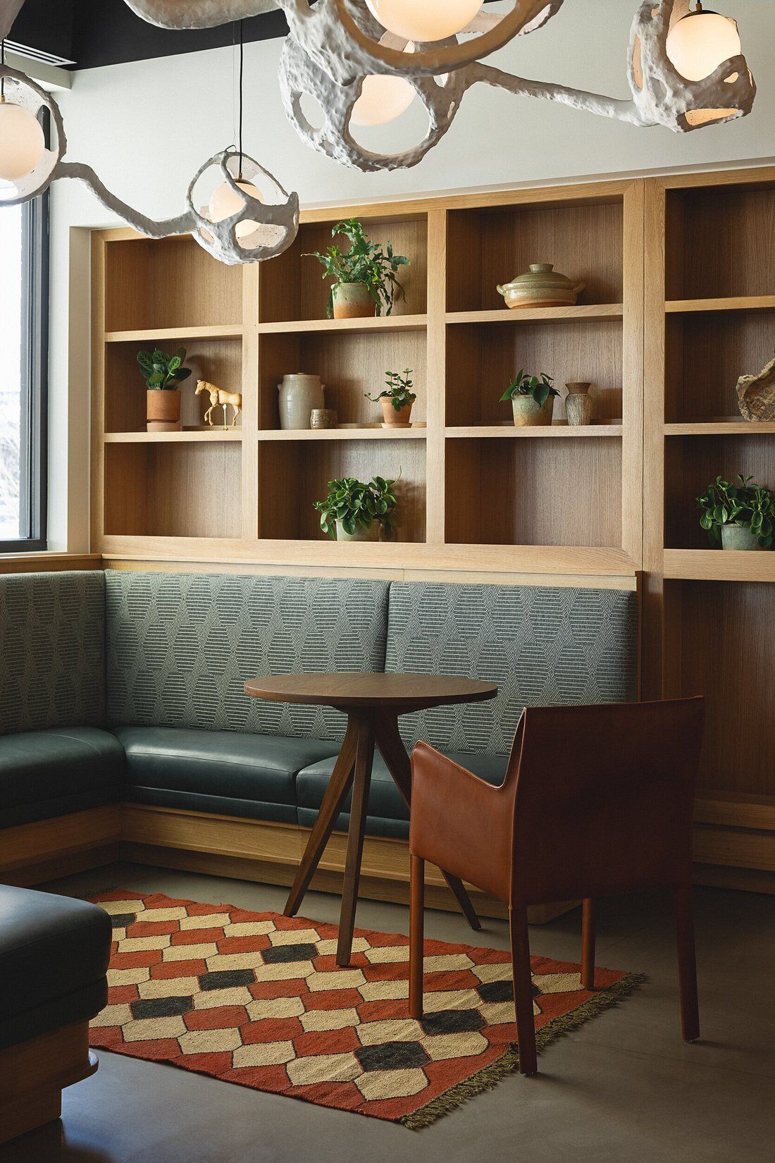 A modern interior with a green upholstered bench, wooden shelving with potted plants, and a round table with a chair.