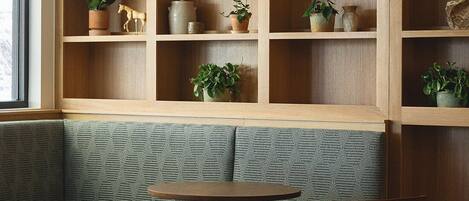 A modern interior with a green upholstered bench, wooden shelving with potted plants, and a round table with a chair.