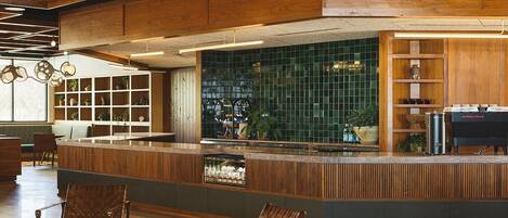 Una zona de bar moderna con mobiliario de madera, un respaldo de azulejos verdes y una estación de parrillada.