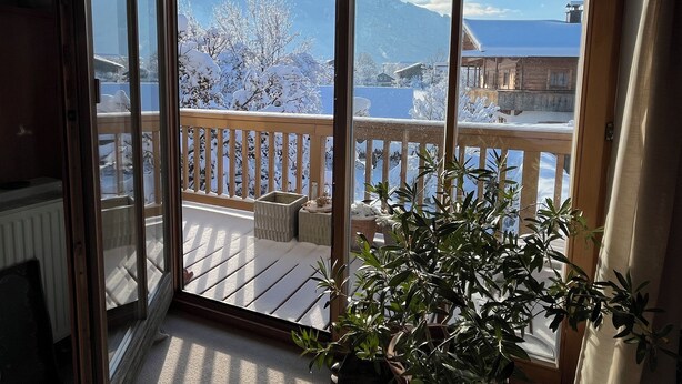 A room with a view of snow-covered mountains and a balcony with a wooden railing. - Ferienwohnung Kampenwinkel 68 qm, Schlafzimmer, Wohn-/schlafzimmer, Südbalkon (Aschau im Chiemgau)