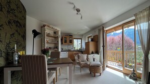 A spacious living area with a dining table, chairs, and a kitchen in the background. - Ferienwohnung Kampenwinkel 68 qm, Schlafzimmer, Wohn-/schlafzimmer, Südbalkon (Aschau im Chiemgau)