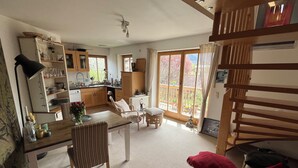 A spacious living area with a dining table, a sofa, and a kitchen in the background. - Ferienwohnung Kampenwinkel 68 qm, Schlafzimmer, Wohn-/schlafzimmer, Südbalkon (Aschau im Chiemgau)