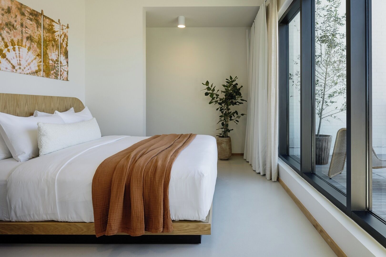 Ein modernes Hotelzimmer mit einem großen Bett, einer Zimmerpflanze und Blick durch ein großes Fenster.