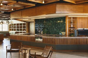 Zona bar moderna con arredi in legno, schienale piastrellato verde e angolo cottura con griglia.