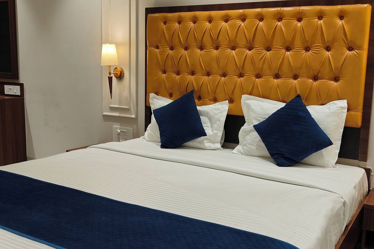 Une chambre d’hôtel avec une tête de lit capitonnée, un grand lit avec une literie blanche et bleue, deux tables de chevet avec des lampes et une table de nuit en bois.