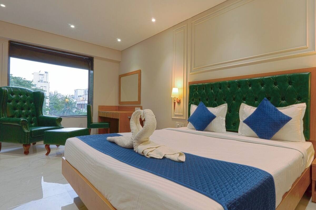 Une chambre d’hôtel avec un grand lit, un fauteuil à revêtement vert et une vue sur la ville par une grande fenêtre.