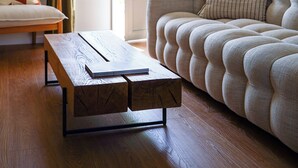 A living room with a sofa, a wooden coffee table, and a view through a glass door.