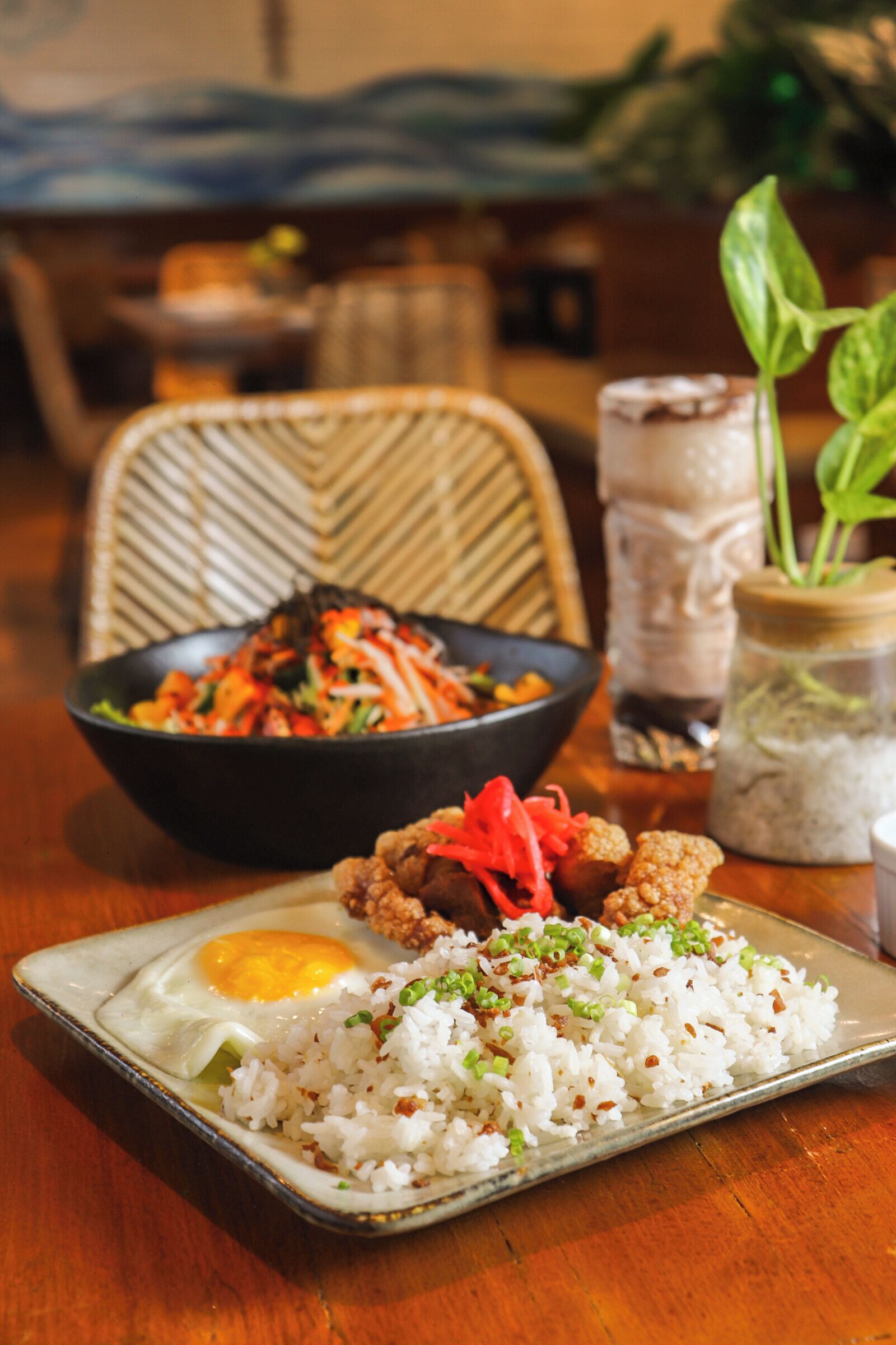 A dining table with a plate of fried rice, a bowl of salad, and a glass of iced tea.