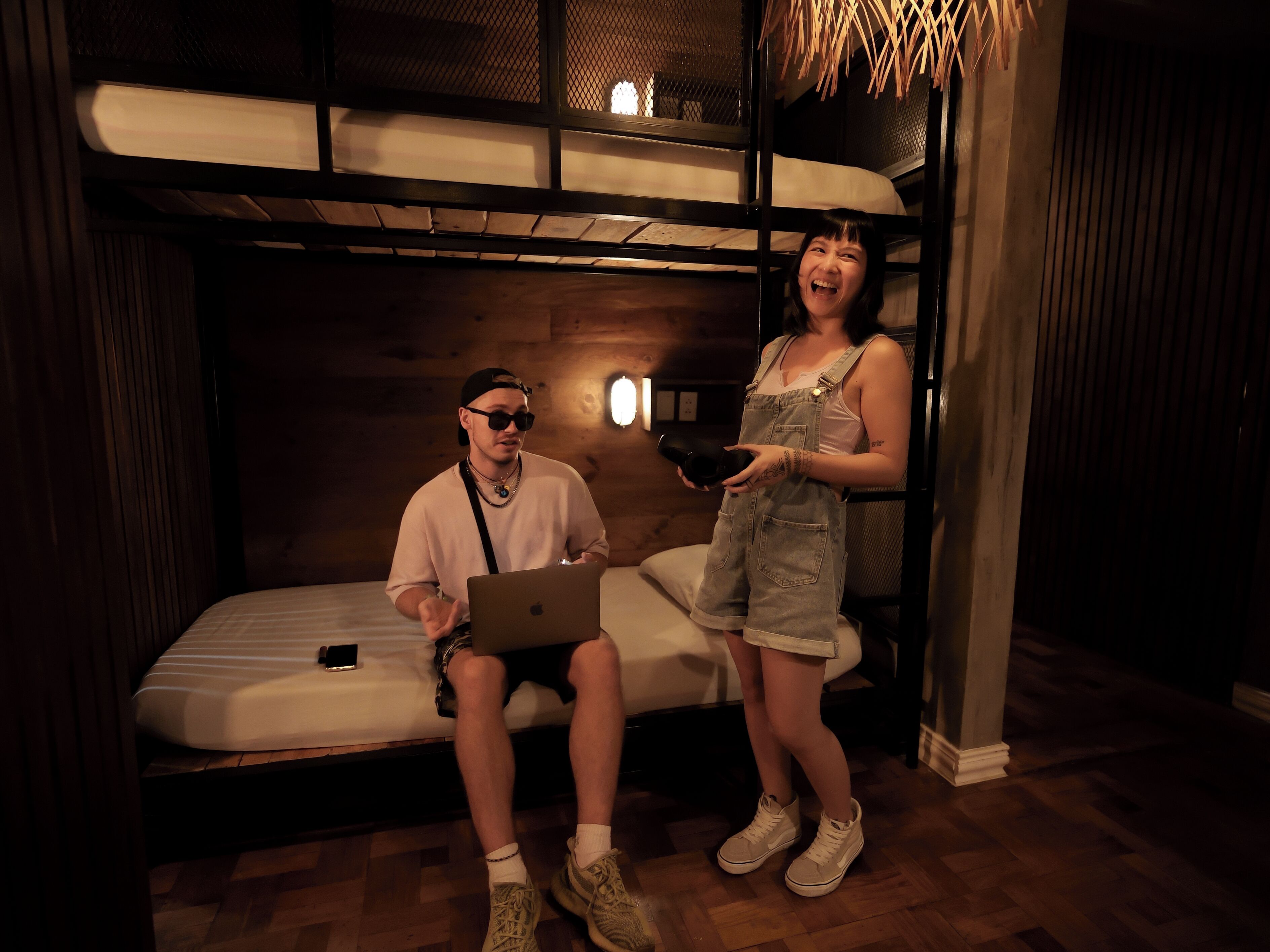 A room with a bunk bed, a laptop on the lower bunk, and a person holding a cup.