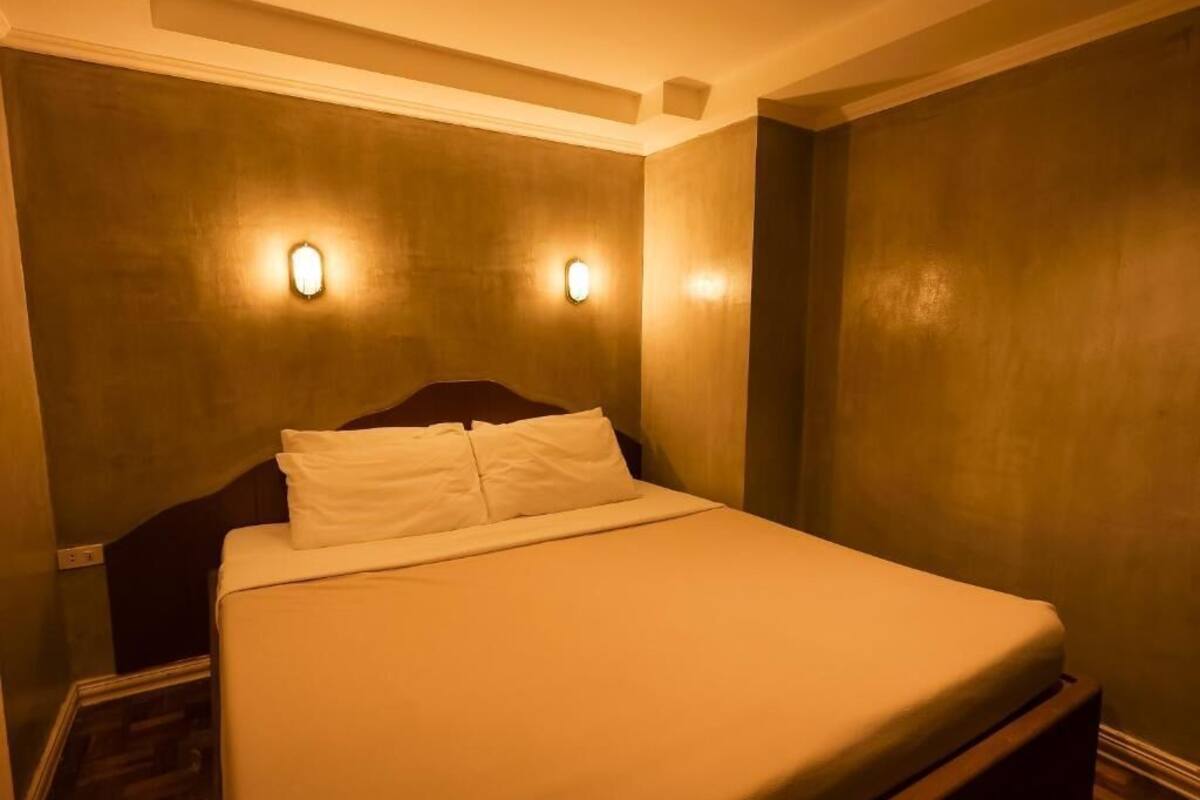 A hotel room with a large bed, two wall-mounted lights, and a wooden headboard.