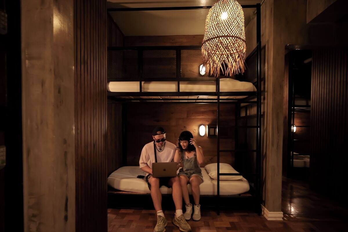 A room with a bunk bed, a laptop on the bed, and a hanging light fixture.