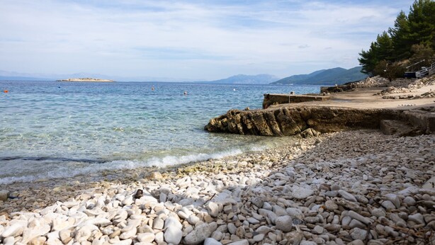 A pebbled beach with clear water, a rocky outcrop, and distant mountains. - Apartments Sea Line (Blato)