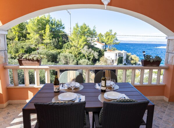 A balcony with a table set for two, overlooking a coastal landscape with trees and buildings. - Apartments Sea Line (Blato)