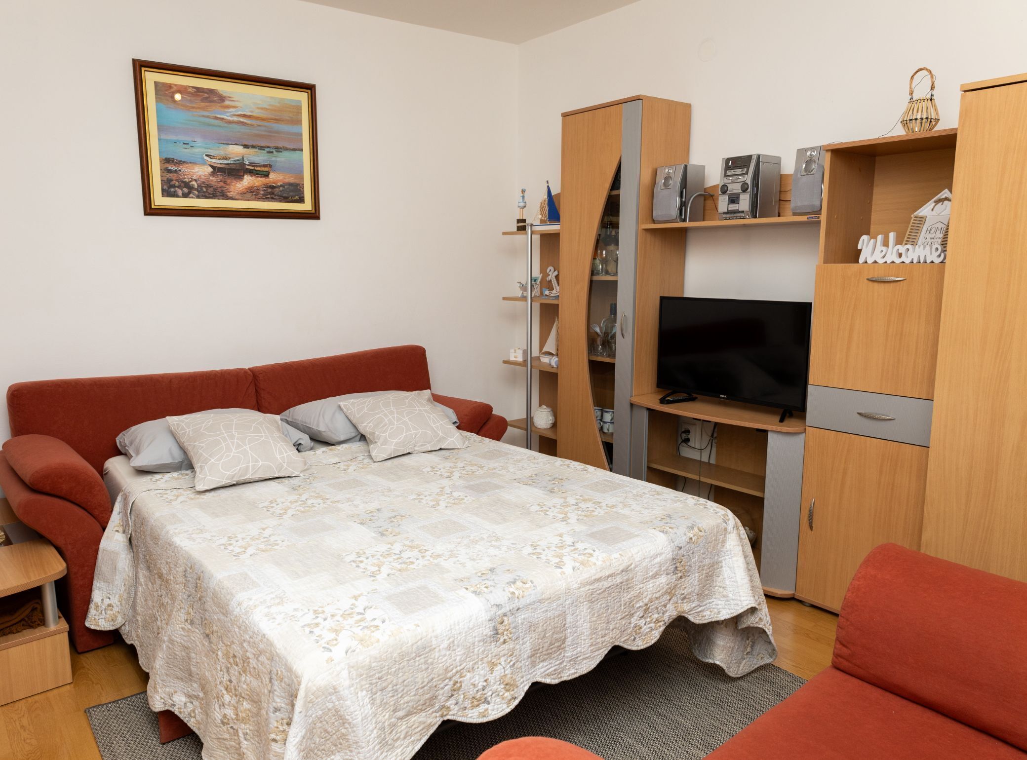 A bedroom with a bed, a TV, a wardrobe, and a painting on the wall.