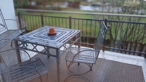 Ein Balkon mit einem Metalltisch und -stühlen, einem kleinen orangen Topf und Blick auf einen Park sowie Gebäude.