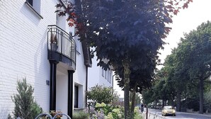Ein Straßenschild mit der Aufschrift 'Herrenwohng' vor einem weißen Gebäude mit einem schwarzen Balkon.
