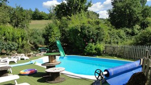 A backyard with a swimming pool, a slide, and a wooden deck. - Maison de Campagne Tilleul (Beynes)