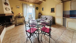 A cozy room with a wooden ceiling, a dining table with four chairs, a sofa, and a kitchen area. - Maison de Campagne Tilleul (Beynes)