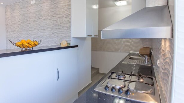 A modern kitchen with a gas stove, white cabinets, and a stone backsplash. - Apartment Mojaš (Dubrovacko Primorje)