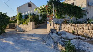 A residential area with a paved driveway leading to a house with a stone wall and a metal gate. - Apartment Mojaš (Dubrovacko Primorje)