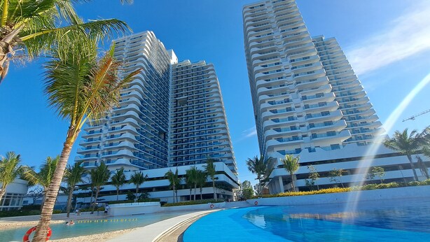 Un hotel moderno con piscina, palmeras y edificios altos al fondo.