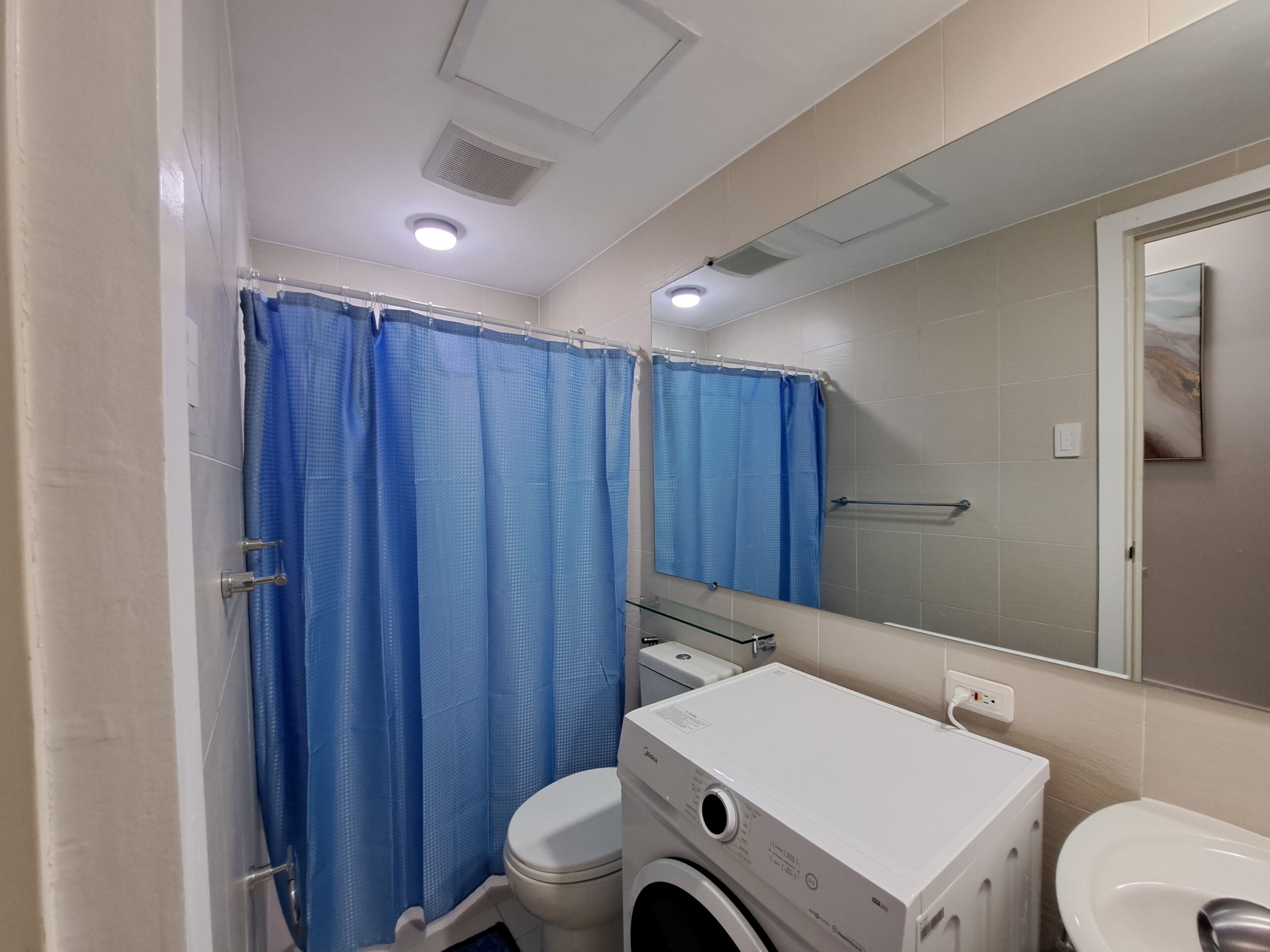 A bathroom with a white toilet, a washing machine, and a blue shower curtain.