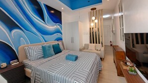 Un dormitorio moderno con una cama grande, un sofá, una mesita de madera y una pared con un cuadro abstracto azul.
