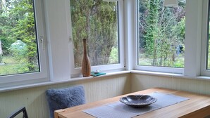 Een eetgedeelte met een houten tafel, een geweven stoel, een blauw kussen en een vaas op de vensterbank.