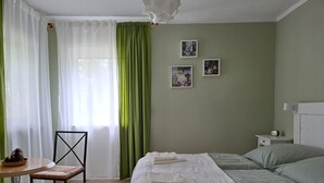 Een slaapkamer met een bed, een stoel, een klein tafeltje en twee ingelijste foto’s aan de muur.