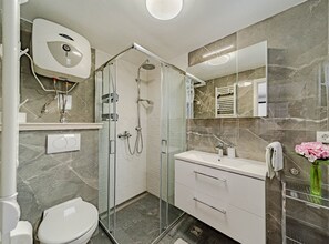 A modern bathroom with a glass-enclosed shower, a white sink, and a marble-tiled wall. - Stone House Blaca (Smokvica)