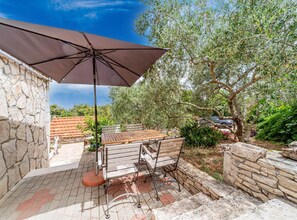 An outdoor patio with a table and chairs, a large umbrella, stone walls, and olive trees. - Stone House Blaca (Smokvica)