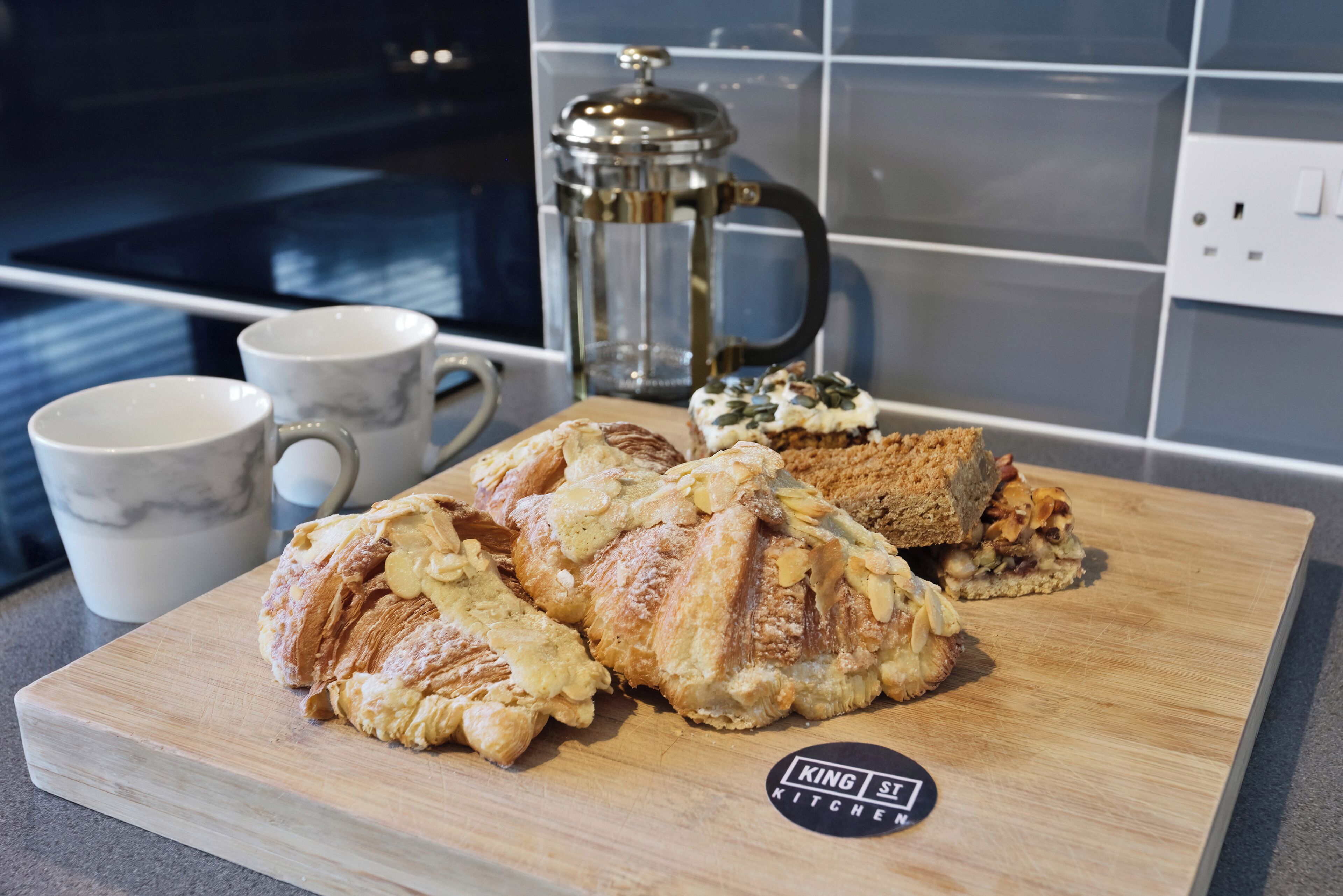 Una tabla de madera con pasteles y una cafetera en una cocina.