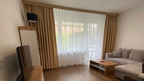 Uma sala de estar moderna com piso de madeira, um sofá, uma mesa de centro e uma TV em um suporte.