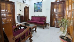 Ein Zimmer mit Holzmöbeln, einem violetten Sofa, einem Glastisch und einem Blumentopf.