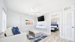 Un salon moderne avec un canapé blanc, une table basse, un téléviseur fixé au mur et un ventilateur de plafond.