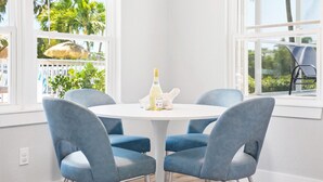 Une table ronde blanche, quatre chaises bleues, une bouteille de vin blanc et un jouet en peluche posés sur la table.