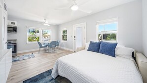 Une chambre avec un lit, un bureau et une chaise, un ventilateur de plafond et des fenêtres donnant sur un paysage verdoyant.