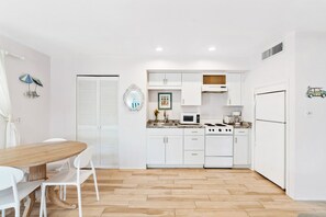 Une cuisine compacte avec des meubles blancs, une cuisinière, un four à micro-ondes et un coin repas comprenant une table en bois et des chaises blanches.
