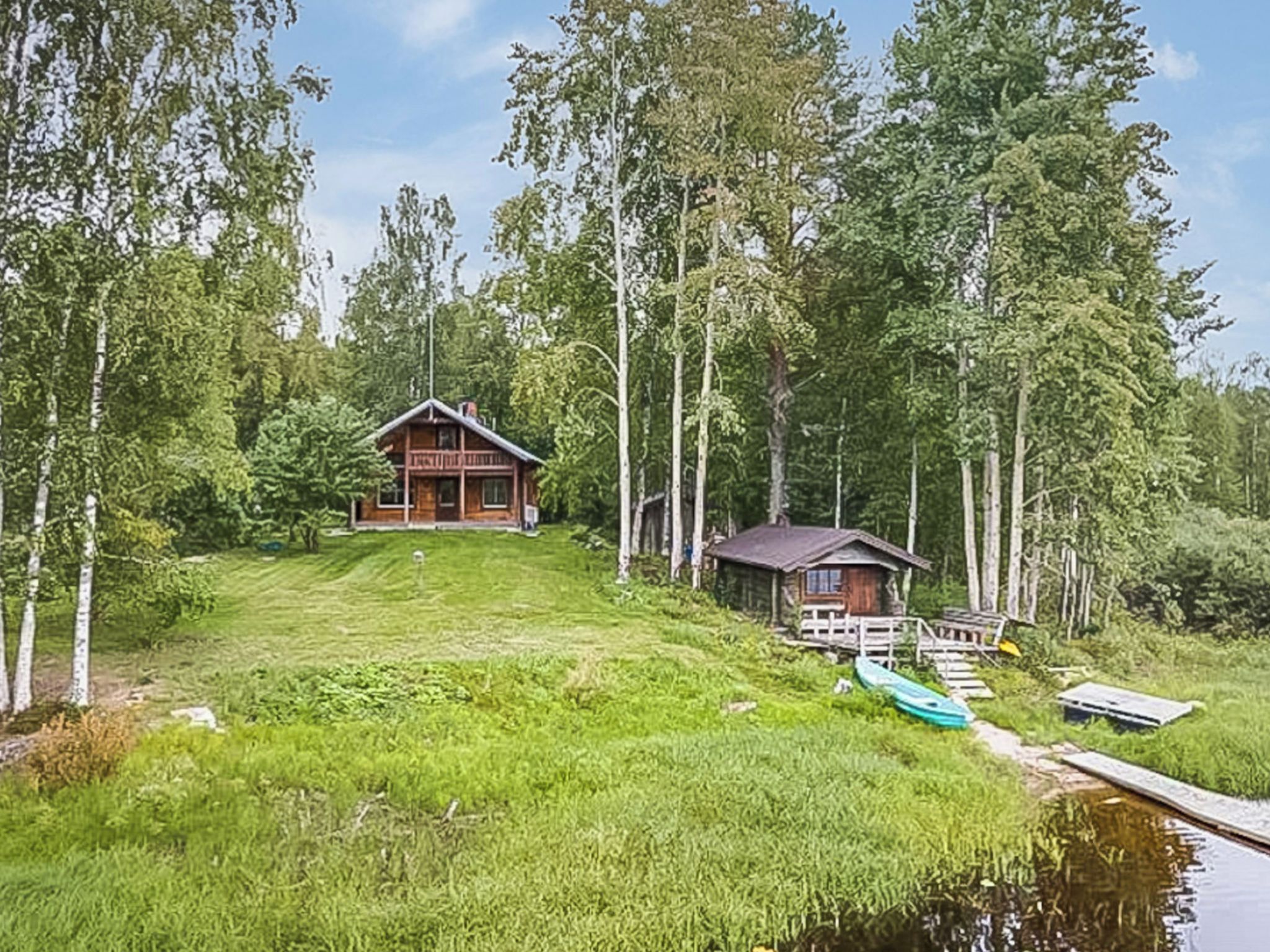 Mökki, jossa on laituri ja pieni vene, ja jonka ympärillä on metsäinen alue.