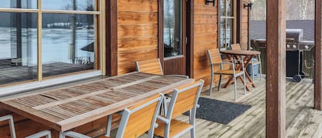 An outdoor wooden deck with a table and chairs, a grill, and large windows.
