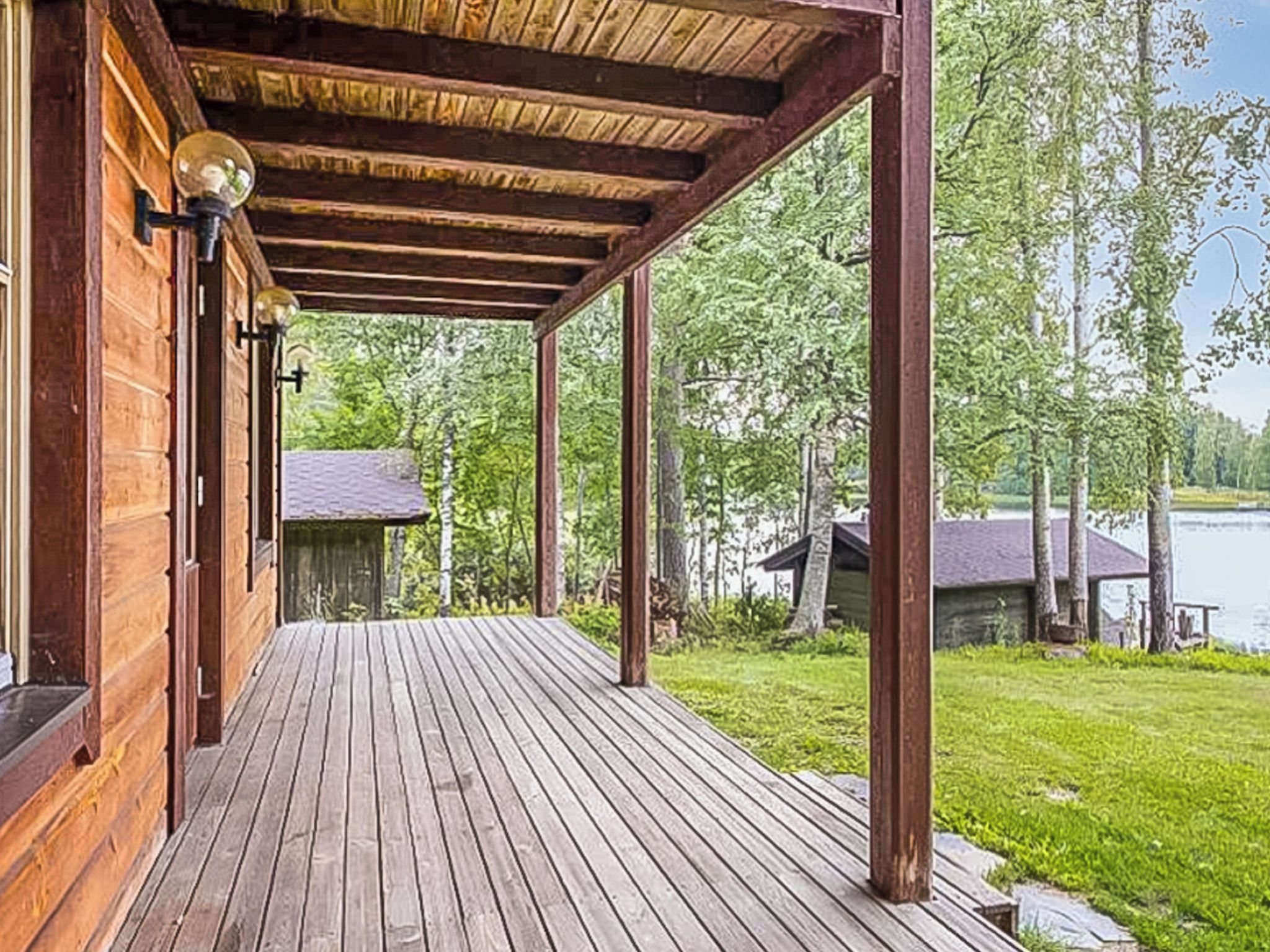 Puinen terassi, jossa on katettu alue, näkymä järvelle ja taustalla pieni rakennus.