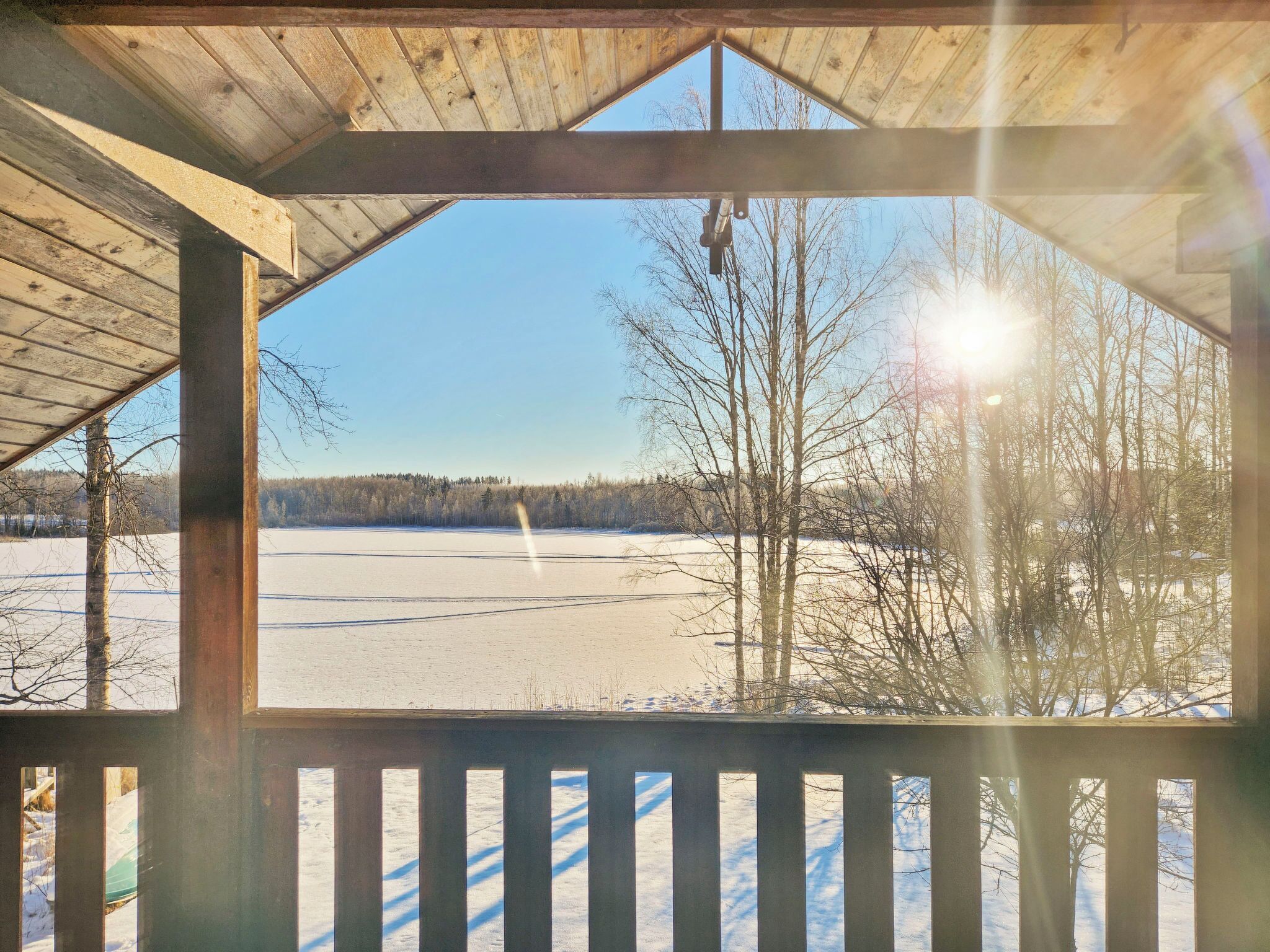A wooden gazebo with a view of a frozen lake and trees.