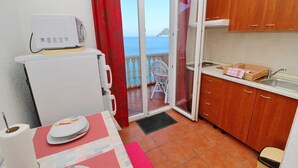 Een kleine keuken met uitzicht op zee, een eethoekje en een balkon met een witte stoel.