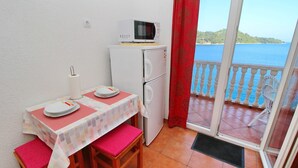 Een klein balkon met uitzicht op zee, een tafel met borden en een magnetron, en een koelkast.