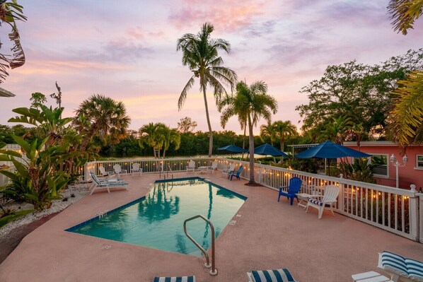 A pool area with lounge chairs and umbrellas, surrounded by palm trees and a fence. - Heated Pool, Dock, Kayaks, Turtle Beach 1-mile & Crescent Beach 2-miles, 1-bdr (Siesta Key)