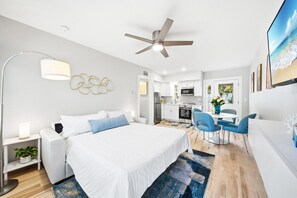 A modern hotel room with a large bed, a desk, a dining area, and a kitchen.