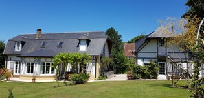 Uma casa de dois andares com um gramado bem cuidado, um alpendre com móveis de exterior e um pequeno jardim com diversas plantas e flores.