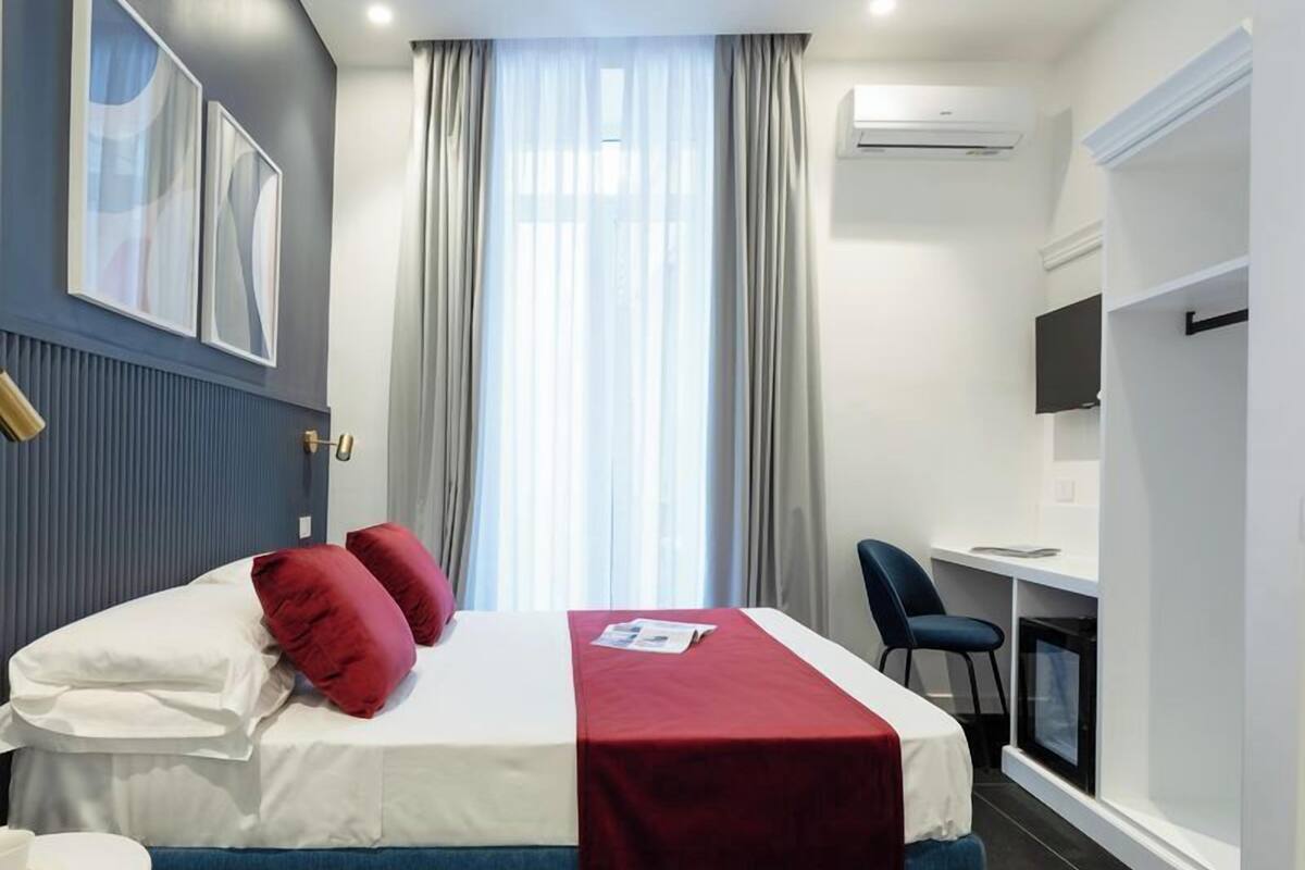 Una habitación de hotel con cama, escritorio, silla, televisor y aire acondicionado.