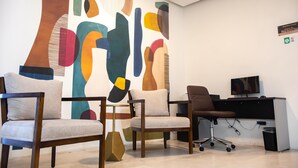Un ufficio moderno con opere d'arte astratte alle pareti, diverse postazioni di seduta tra cui un divano e poltrone, una scrivania con un computer e un cestino.