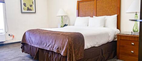 A neatly made bed with a brown bedspread and white pillows, a wooden headboard, a bedside table with a lamp, and a framed picture on the wall.
